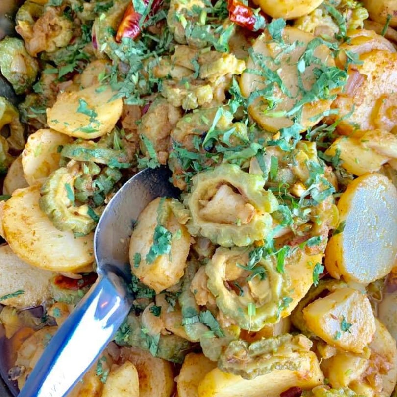 Close-up of Nepalese bitter melon and potato curry, garnished with fresh cilantro and a serving spoon.