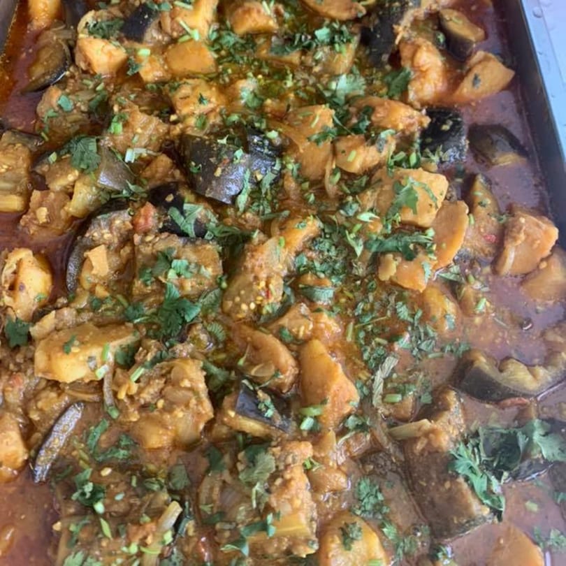 Close-up of a Nepalese dish with potatoes, eggplant, and cilantro in a rich sauce.