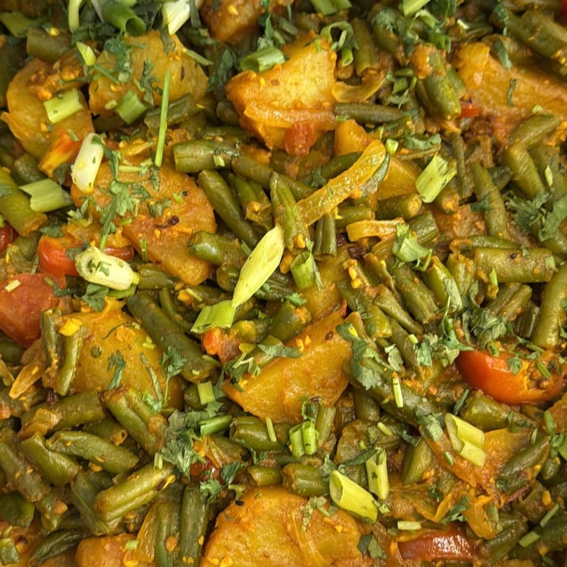 Close-up of a Nepalese dish with green beans, potatoes, tomatoes, and herbs.
