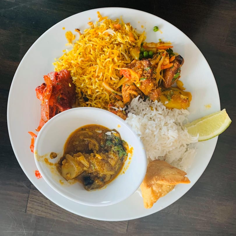 A white plate with a variety of Nepalese dishes, including rice, curry, and samosas.