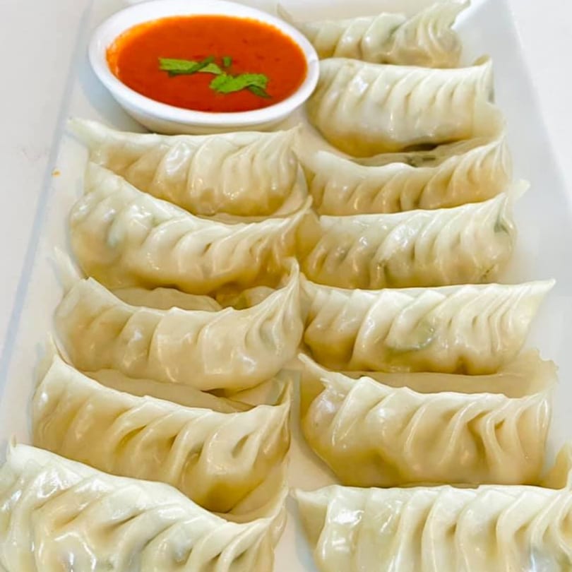A plate of Kathmandu Restaurant's Nepalese momo dumplings with a side of red dipping sauce.