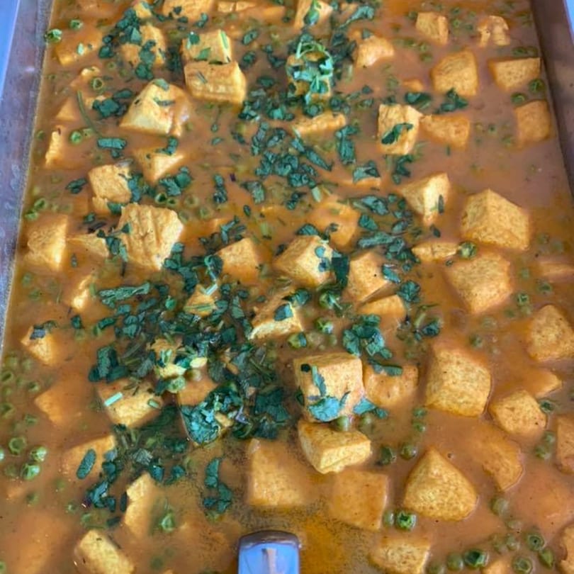 Close-up of Kathmandu Restaurant's paneer curry with peas and fresh herbs in a serving tray.