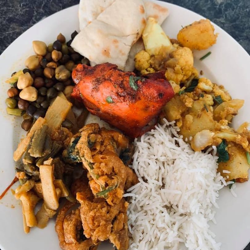 A plate of Nepalese food with rice, naan, chicken, chickpeas, and vegetables.