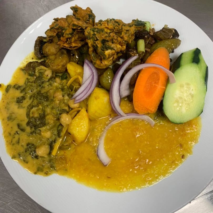 A Nepali dish with fried pakora, curried vegetables, dal, and fresh cucumber and carrot slices.